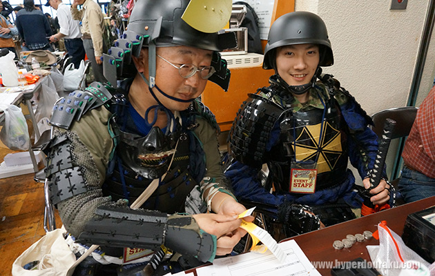 陸自迷彩に戦国甲冑を重ね着する券売スタッフ